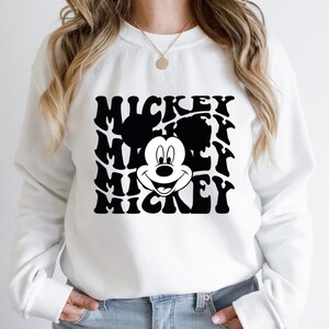 May include: White sweatshirt with a black and white graphic of Mickey Mouse's face and the word "Mickey" repeated in a wavy pattern.