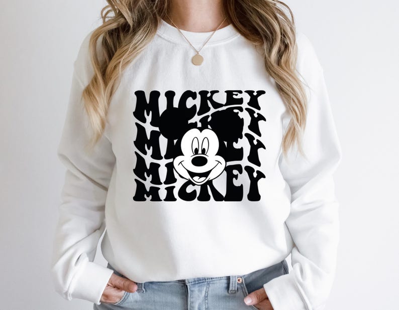 May include: White sweatshirt with a black and white graphic of Mickey Mouse's face and the word "Mickey" repeated in a wavy pattern.