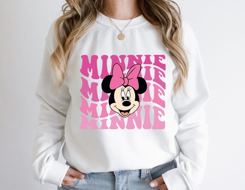 K&ouml;nnte beinhalten: Wei&szlig;er Pullover mit einem pinkfarbenen und wei&szlig;en Aufdruck von Minnie Mauss Gesicht und dem Wort "Minnie", das in einer Retro-Schrift wiederholt wird.