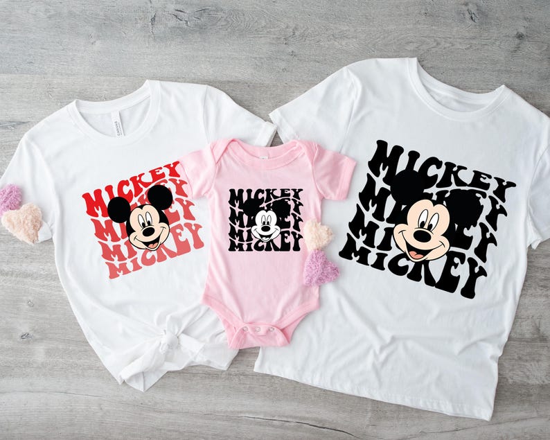 May include: Three white t-shirts with a black and white Mickey Mouse graphic and the word "Mickey" repeated in red and black. The shirts are in different sizes, with the smallest shirt being pink.