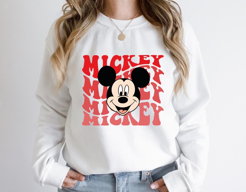 May include: White sweatshirt with a red and pink graphic of Mickey Mouse's face and the word "Mickey" repeated multiple times.