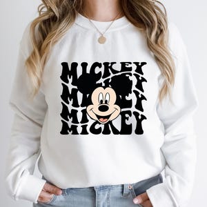 May include: White sweatshirt with a black and white graphic of Mickey Mouse's face with the word "Mickey" repeated in a wavy pattern.