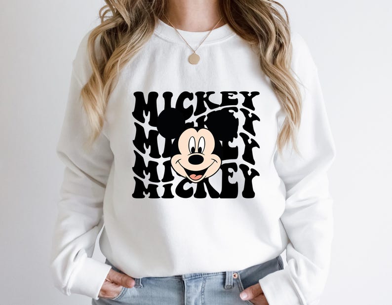 May include: White sweatshirt with a black and white graphic of Mickey Mouse's face with the word "Mickey" repeated in a wavy pattern.