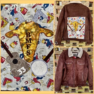 May include: A brown suede jacket with a sherpa collar and a patch on the back. The patch is a colourful design with a guitar, a banjo, and the letters "BMFS" in the centre. The jacket has a zip closure and two pockets on the front.