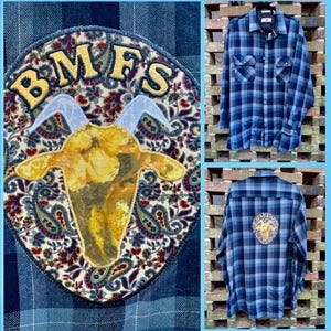 May include: A blue and white plaid flannel shirt with a patch on the front. The patch is a paisley design with a goat head in the center and the text "BMFS" above the goat.