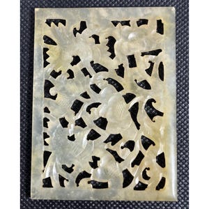 May include: A white jade carving with intricate openwork design featuring floral motifs. The carving is rectangular and has a smooth, polished surface.