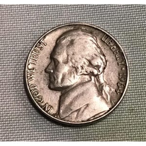 May include: A silver US half dollar coin with the profile of Thomas Jefferson on the obverse. The coin reads "IN GOD WE TRUST" and "LIBERTY 1964".