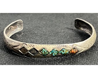 May include: A silver bracelet with a geometric design and inlaid turquoise, black, and orange stones.