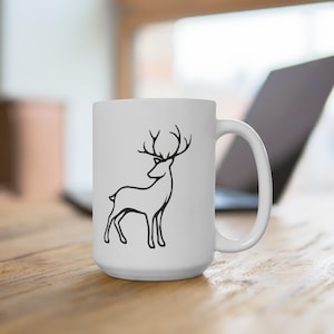 May include: White ceramic coffee mug with a black outline of a deer with antlers. The mug is on a wooden table.
