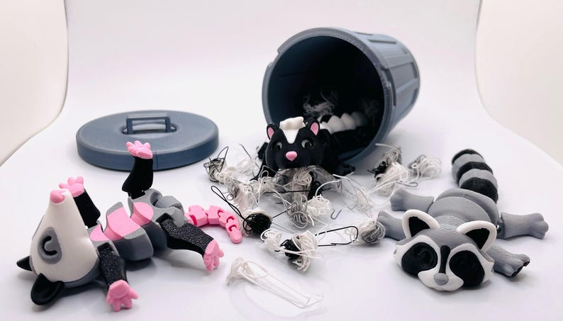 Op de afbeelding: Een grijze plastic prullenbak met een deksel is omgevallen en laat wit, draderig materiaal eruit vallen. Er zijn drie kleine dierenfiguren: een wasbeer, een stinkdier en een opossum. Het opossum ligt op zijn rug met zijn poten in de lucht.