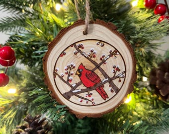 May include: A wooden Christmas ornament featuring a hand-painted cardinal perched on a branch with red berries. The ornament is a natural wood slice with a rustic finish.