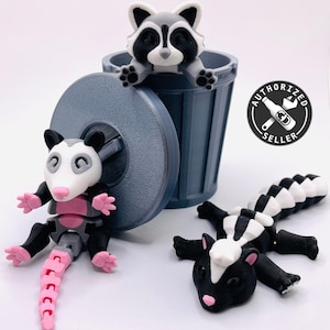 Op de afbeelding: Drie 3D-geprinte dierenfiguren: een wasbeer in een grijze prullenbak, een opossum met een roze staart en een stinkdier met een zwart-wit gestreepte staart.