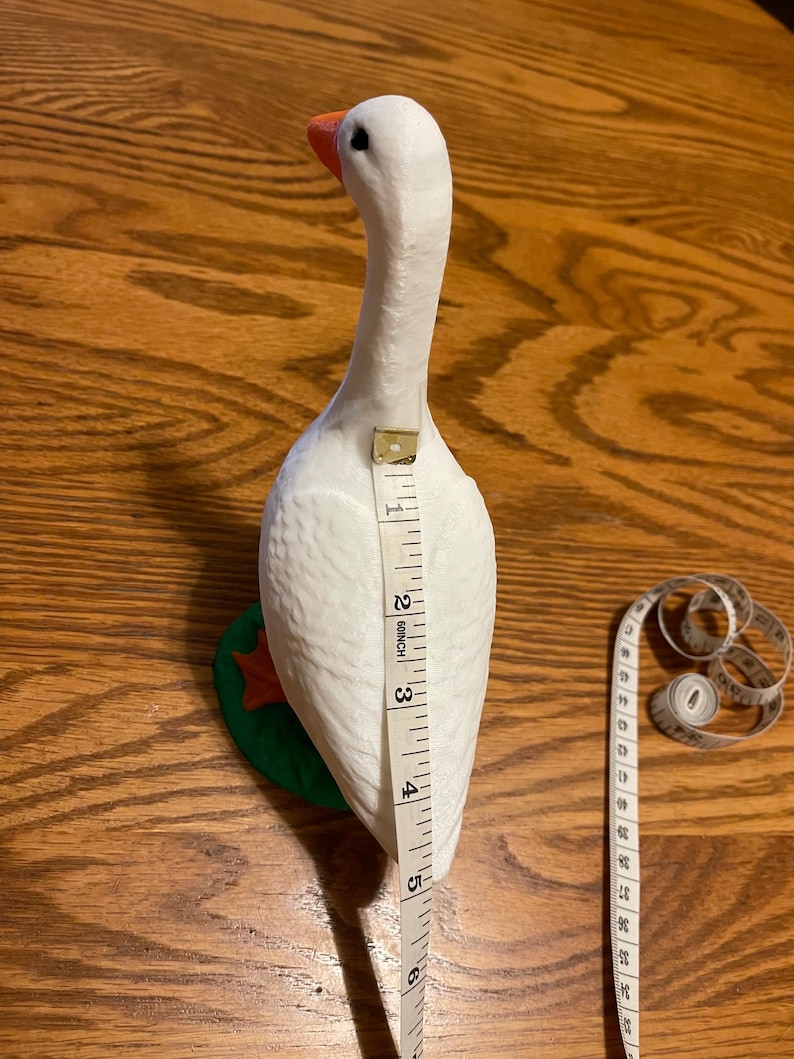 K&ouml;nnte beinhalten: Wei&szlig;e G&auml;nsefigur mit gr&uuml;nem Sockel, gemessen mit einem Ma&szlig;band, 15 cm hoch.