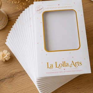 Pode incluir: Uma pilha de capas de embalagem de papel branco retangulares com uma janela central recortada. A frente apresenta texto dourado lendo La Lolla Arts, Personalized Party & Paper Craft Studio e Little details for special celebrations.