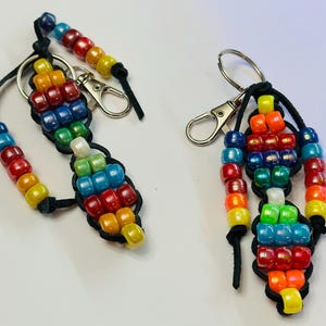 May include: Two colorful beaded keychains with rainbow colored beads and silver key rings. The keychains are made with black leather cord.