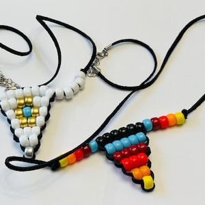 May include: Two beaded necklaces with black cord. One necklace has white and gold beads in a triangular pattern with a turquoise center bead. The other necklace has black, blue, red, orange, and yellow beads in a triangular pattern.