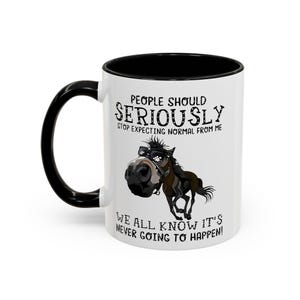 May include: White ceramic mug with a black interior and handle. The mug features a cartoon horse with a large nose and text that reads "PEOPLE SHOULD SERIOUSLY STOP EXPECTING NORMAL FROM ME. WE ALL KNOW IT'S NEVER GOING TO HAPPEN!"