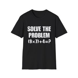 May include: Black t-shirt featuring the white text "SOLVE THE PROBLEM" and the mathematical equation (9x7)+4=? The short-sleeved top has a crew neck. The text has a distressed effect, giving it a vintage look.