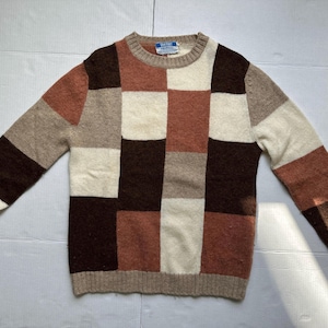 May include: A vintage patchwork sweater in shades of brown, beige, and cream. The sweater has a crew neck and long sleeves with ribbed cuffs. The body of the sweater is made up of large, rectangular blocks of colour.