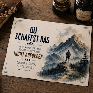 Könnte beinhalten: Eine rechteckige Karte mit einer Aquarellillustration einer Person, die auf einem Bergpfad steht und auf ein Gebirge blickt. Der Text lautet: DU SCHAFFST DAS, AUCH WENN DER WEG GERADE SCHWER IST: NICHT AUFGEBEN. DU BIST STÄRKER, ALS DU DENKST. Die Karte ist cremefarben.