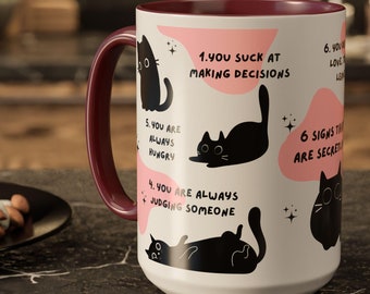 Puede incluir: Taza de cerámica blanca con borde marrón. La taza presenta una ilustración en blanco y negro de gatos con texto que dice "1. You suck at making decisions", "4. You are always judging someone", "5. You are always hungry", y "6 signs that you are secretly a cat".
