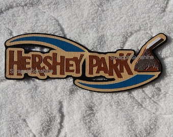 May include: Hershey Park logo patch with a brown Hershey's Kiss on a tan background with blue accents.