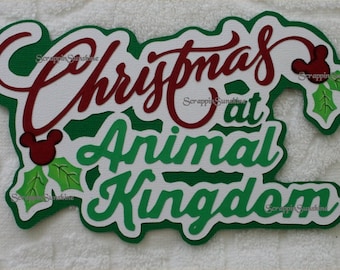Puede incluir: Señal de Navidad verde y roja "Christmas at Animal Kingdom" con orejas de Mickey Mouse y hojas de acebo.