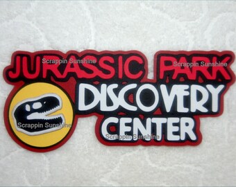 May include: Red and black Jurassic Park Discovery Center logo with a yellow circle containing a black dinosaur silhouette.