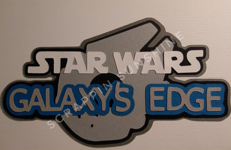 Puede incluir: Una manualidad de papel blanca y gris con el texto "Star Wars Galaxy's Edge" en letras negras y azules. La manualidad tiene forma de nave espacial.