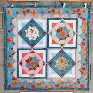 May include: A colorful quilt with a floral design, featuring squares of teal, pink, and white, adorned with orange poppy accents. The quilt is displayed on a wooden hanger. Text on the quilt reads "Poppy Louise" and "Bold Curves - Brilliantly Simple".