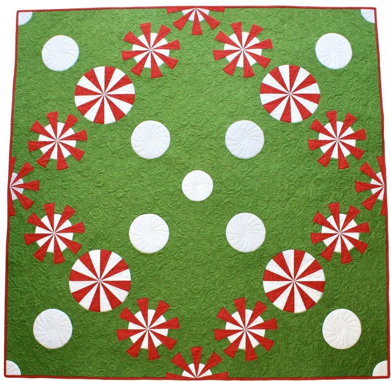 May include: A green quilt with a red border, featuring a pattern of white circles and red and white pinwheel designs. The quilt has a textured surface and is likely handmade.