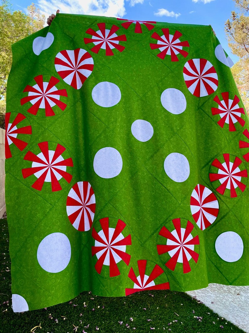 May include: A green quilt with a pattern of large white polka dots and red and white pinwheel designs. The quilt is made of a soft fabric and has a quilted texture. The overall theme is festive and whimsical.