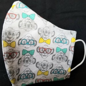 May include: White face mask with a repeating pattern of cartoon lion faces wearing glasses and bow ties. The glasses are in red, blue, and green. The bow ties are yellow, blue, and green.