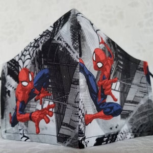 May include: A gray, black, and red face mask with a Spiderman design. The mask features a cityscape background with Spiderman swinging through the city.