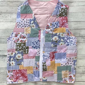 May include: A sleeveless vest featuring a patchwork design of various floral, gingham, and striped fabric squares in shades of pink, blue, yellow, green, and red. The garment has a white front zipper closure and a solid light pink interior lining.