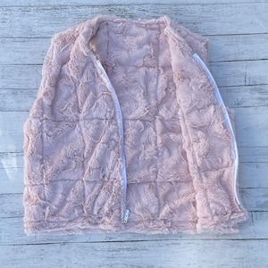May include: A pink faux fur vest with a zipper closure. The vest is quilted and has a soft, plush texture.