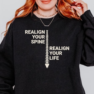 May include: Black sweatshirt with a white graphic of a spine and the text "Realign your spine, Realign your life".