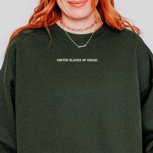 May include: Dark green sweatshirt with the text "UNITED SLAVES OF ISRAEL" in white. The sweatshirt is a solid color and has a crew neck. The image shows the upper body of a person wearing the sweatshirt.