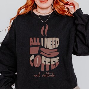 May include: Black sweatshirt with a graphic design of a coffee cup and the text "All I need is coffee and solitude".