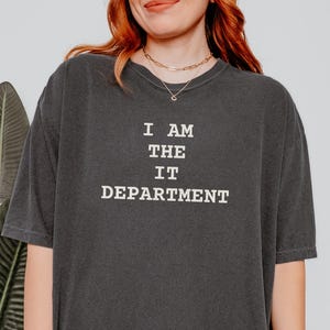 May include: A dark gray t-shirt with the text "I AM THE IT DEPARTMENT" printed in white.