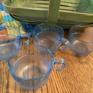 May include: Four blue plastic cups with handles. The cups are translucent and have a frosted finish. The cups are sitting on a wooden surface.