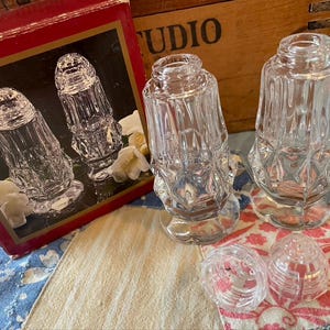 May include: Clear glass salt and pepper shakers with a diamond pattern. The shakers have a classic design and come with matching lids. The image also shows the original box with a picture of the shakers.