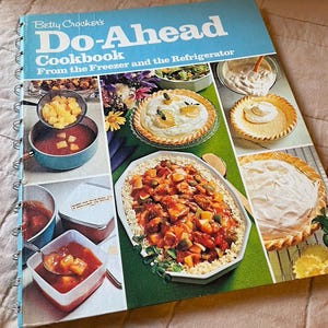 May include: A vintage cookbook titled "Betty Crocker's Do-Ahead Cookbook" with a blue cover and spiral binding. The cover features images of prepared dishes, including pies and stews. The cookbook is open, displaying colorful food photography.