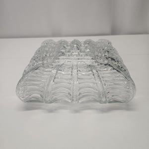 Pode incluir: Um objeto decorativo quadrado de vidro transparente com um design texturizado e com nervuras. O vidro tem uma textura borbulhante na superfície superior e uma série de cristas verticais nas laterais. Um objeto decorativo para casa.