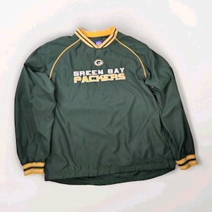 Könnte beinhalten: Dunkelgrüne Green Bay Packers Pullover-Jacke mit goldenen und weißen Akzenten. Der Schriftzug und das Logo des Teams sind in Gold gehalten. Kragen und Manschetten sind gold-weiß gestreift.