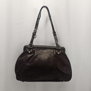 May include: A dark brown leather handbag with two handles and silver-tone hardware. The bag has a rounded shape with a structured top and a zipper closure. The handles are adjustable and attached with buckles.