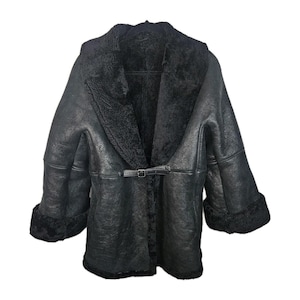 May include: A black shearling coat with a wide collar and a buckle closure. The coat features a plush, black interior lining and cuffs. The exterior has a textured appearance, and the coat is designed for warmth and style.