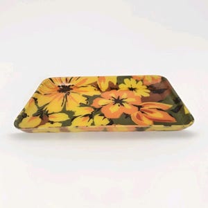 Può includere: Un vassoio rettangolare con un motivo floreale. Il vassoio presenta grandi fiori gialli e arancioni con foglie marroni e verdi su uno sfondo verde scuro. Il vassoio ha un bordo leggermente rialzato e una finitura lucida.