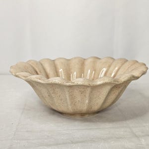 以下が含まれることがあります： ベージュ色のセラミックボウル、スカラップリム付き。 ボウルは斑点のあるテクスチャで、幅が広く浅いデザインです。 リムは波状の、花びらのような形をしています。 ボウルは、サービングまたはディスプレイ用です。