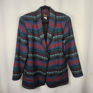 Puede incluir: Una blazer vintage con un colorido estampado geométrico en tonos rojos, turquesa, azul y negro. La blazer tiene un cierre de un solo botón y un cuello con muescas. La etiqueta dice "Pin La New York".